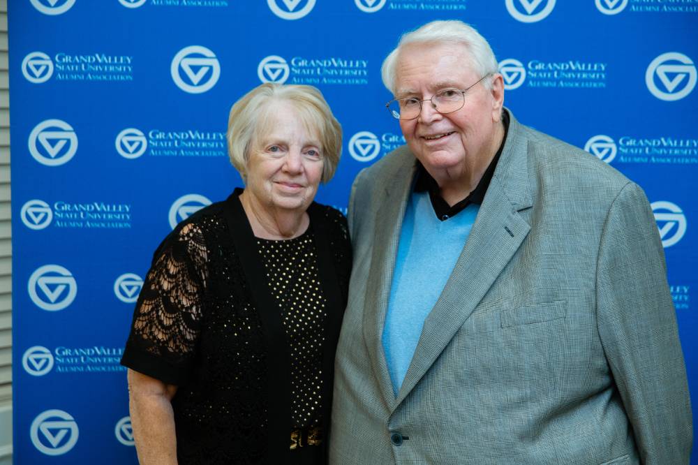 Two alumni pose for a photo together with the blue Grand Valley backdrop behind them at the Reunion Dinner.